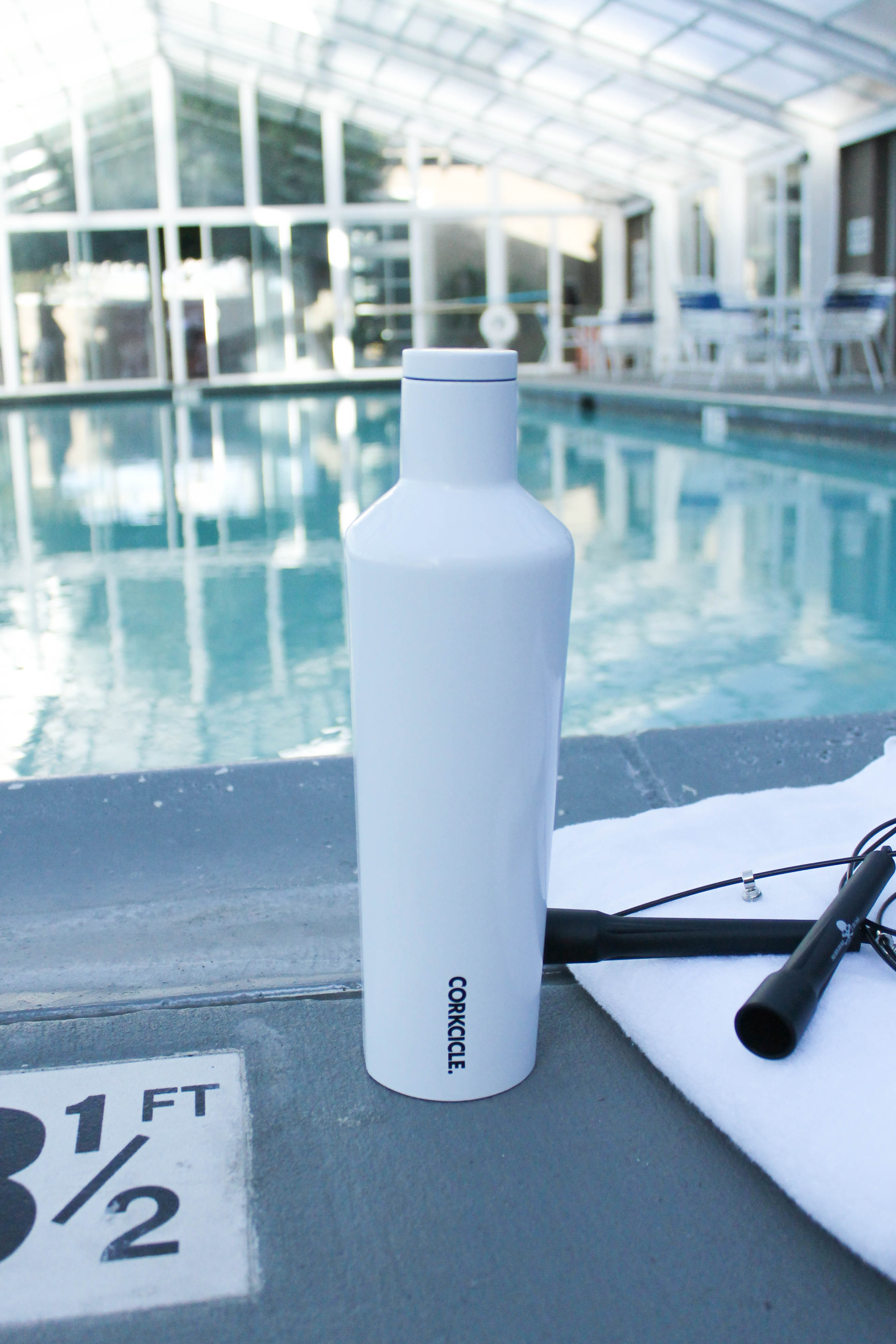 Workout am Pool mit weißer Wasserflasche von Corkcicle, Springseil und Handtuch